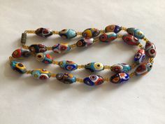 "This long necklace of handmade millefiori glass beads and cut crystal beads gives a fresh fashion spin to your boho look, your jeans or your little black dress. Ravishing color is fused in these oval beads blues, red, orange, greens, aqua and sun yellow. Faceted link chain and metal accents are finished in bronze. Millefiori means \"thousand flowers.\" Bundles of tiny glass filament rods are sliced, then fired to meld their brilliant colors and floral patterns. No two beads are ever identical." Bohemian Murano Glass Round Bead Necklaces, Bohemian Handmade Murano Glass Necklaces, Bohemian Murano Glass Beaded Necklaces, Bohemian Murano Glass Beads, Colorful, Bohemian Handmade Murano Glass Necklace, Bohemian Murano Glass Beaded Necklace, Handmade Oval Glass Necklace, Bohemian Murano Glass Colorful Beads, Bohemian Colorful Murano Glass Beads