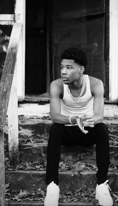 a black and white photo of a young man sitting on steps with his hands in his pockets