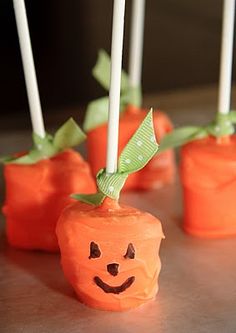 candy apples decorated like pumpkins with green bows and faces on them, sitting on a table