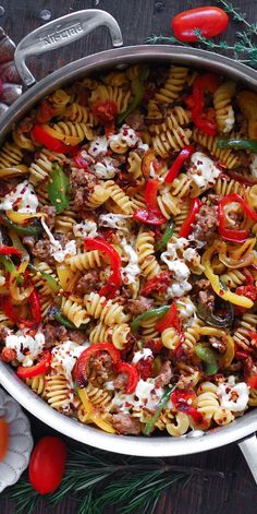 a pot filled with pasta and vegetables on top of a wooden table next to tomatoes