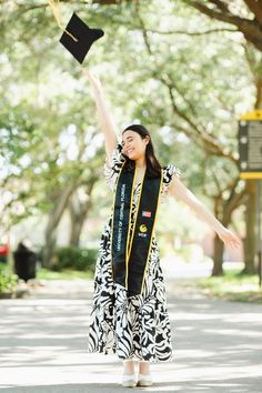 a woman in a black and white dress is throwing her graduation cap into the air