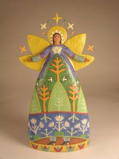 an angel figurine sitting on top of a white surface with trees and stars around it