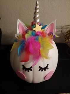 a white pumpkin decorated with colorful feathers and a unicorn's face