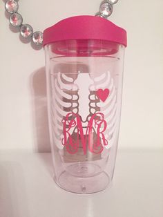 a clear cup with pink lid sitting on top of a white table next to a beaded necklace