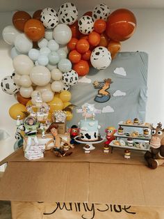 a table topped with lots of balloons and cake next to a wall covered in animals