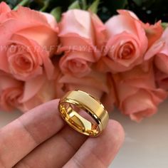 a hand holding a gold wedding ring next to pink roses