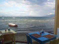 a table and chairs on the beach with boats in the water