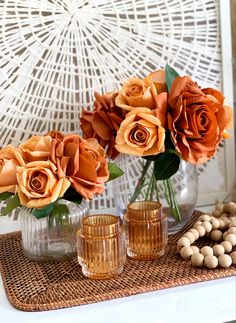 three vases filled with orange roses on top of a wicker table cloth next to cookies