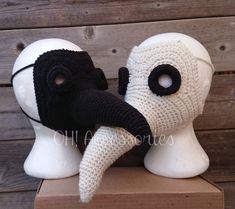 two white and black knitted masks sitting on top of a wooden box next to each other