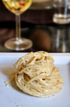 a white plate topped with pasta next to a glass of wine