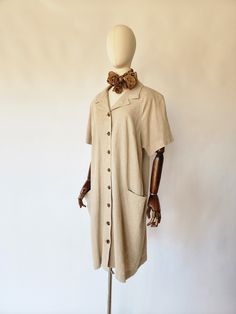 Vintage shirt dress is quintessential 1980's. It is made of a khaki linen fabric and is very comfrontable. The dress features a v-neckline, a chic neckscarf, short sleeves, side hip pockets, a hemline that falls below the knee, and tortise brown colored button down closures at the front. A great work dress and addition to any wardrobe. size: best fits, US medium bust - 46 inches waist -47 inches sleeves - 15 inches hips - 48 inches length - 41 inches scarf: 41 inches long material - linen, butto Collared Beige Linen Shirt Dress, Beige Collared Linen Shirt Dress, Beige Linen Collared Shirt Dress, Collared Beige Cotton Shirt Dress, Beige Linen Button-up Shirt Dress, Beige Relaxed Fit Shirt Dress With Buttons, Oversized Vintage Summer Dress, Beige Linen Shirt Dress With Button Closure, Beige Button-up Linen Summer Dress