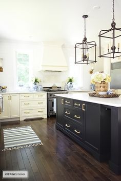 a kitchen with black and white cabinets, wood flooring and chandelier hanging from the ceiling