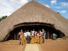 a group of people standing in front of a thatched roof structure with words written below it