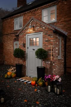 a brick house with potted plants and pumpkins in the front yard at night