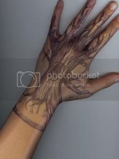 a person's hand with tattoos on it holding an object in the shape of a tree