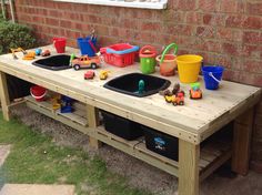 a wooden table with two black sinks and toys on the top, in front of a brick wall