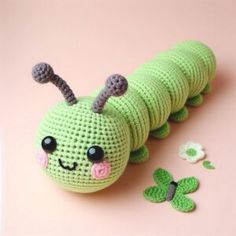 a green crocheted caterpillar with eyes and nose sitting on a pink surface