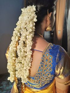 a woman wearing a yellow and blue sari with flowers in her hair, back view