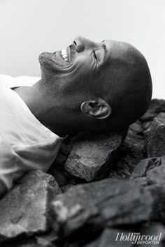 a black and white photo of a man laying on rocks with his eyes closed looking up