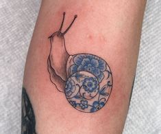 a tattoo with a snail on it's leg and blue flowers in the background