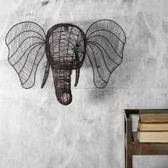 an elephant head made out of wire hanging on the wall next to a stack of books