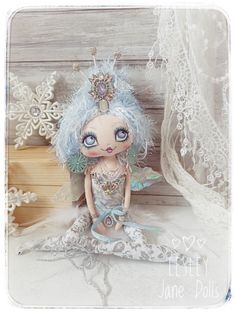 a small doll sitting on top of a bed next to a wooden wall with white lace