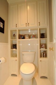 a white toilet sitting inside of a bathroom next to a cabinet filled with books and other items