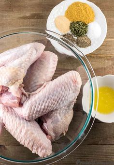 raw chicken in a glass bowl with spices and seasoning on the side next to it