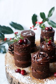 small chocolate cakes with frosting and cranberries on a wooden board surrounded by holly leaves