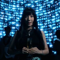 a woman holding a wine glass in front of a blue wall with lights on it