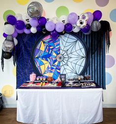 a table topped with lots of purple and white balloons next to a wall covered in disco balls