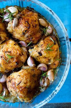 chicken with garlic and herbs in a glass dish on a blue tablecloth, ready to be eaten