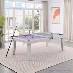 a pool table in a living room next to a potted plant and large windows