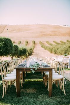 a wooden table with white chairs and flowers on it in front of an outdoor seating area