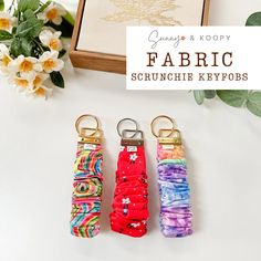 three keychains are sitting next to each other on a white surface with flowers in the background