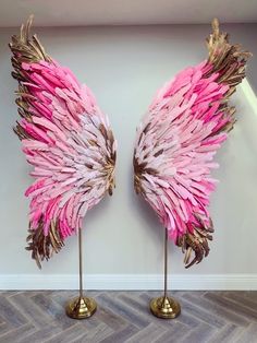 two pink and gold angel wings sitting on top of each other in front of a white wall