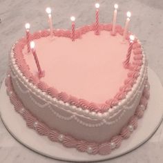 a heart shaped cake with lit candles on it's top and pink frosting