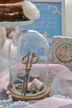 there is a cake under a glass dome with scissors and thread on the table next to it