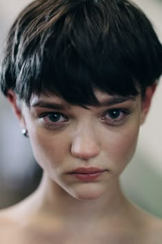 a close up of a woman with short hair and piercings on her ears looking at the camera