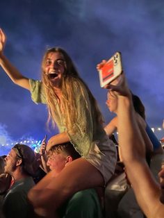 a woman is holding up her cell phone in the air as she sings at an outdoor concert