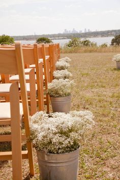 several buckets filled with white flowers sitting on top of a grass covered field next to wooden chairs