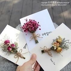 three cards with flowers tied to them and someone holding one in their hand next to each other