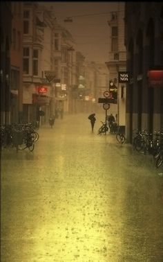 a city street is flooded with water and people are walking down the sidewalk in the rain