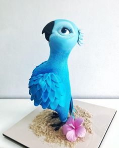 a blue bird statue sitting on top of a white plate next to a pink flower