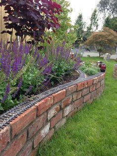 a brick garden wall with flowers and plants growing on it's sides in the grass