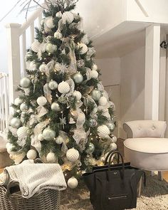 a white christmas tree with silver ornaments in a living room next to a black bag