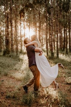 a man and woman are hugging in the middle of a forest with pine trees behind them