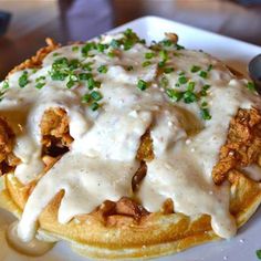 a waffle covered in gravy and topped with green onions on a white plate