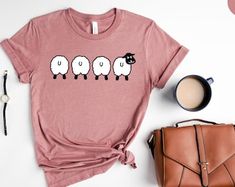 a t - shirt with three sheep on it next to a purse and coffee cup