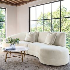 a living room with large windows and a white couch in front of a table on top of a rug